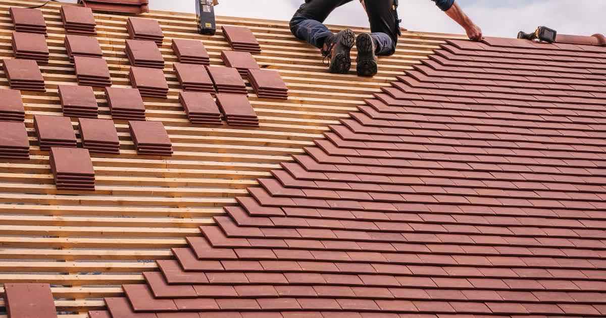 Dakwerker legt rode dakpannen op een hellend dak