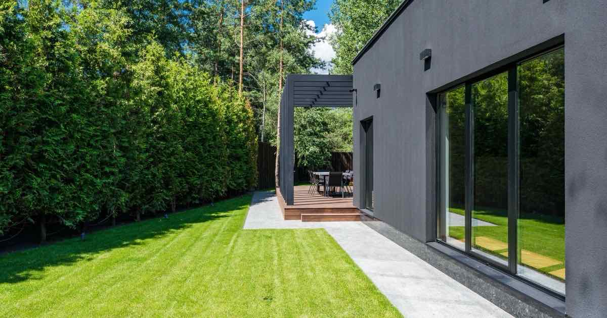 Pad van betontegels langs een gazon en een moderne donkere woning