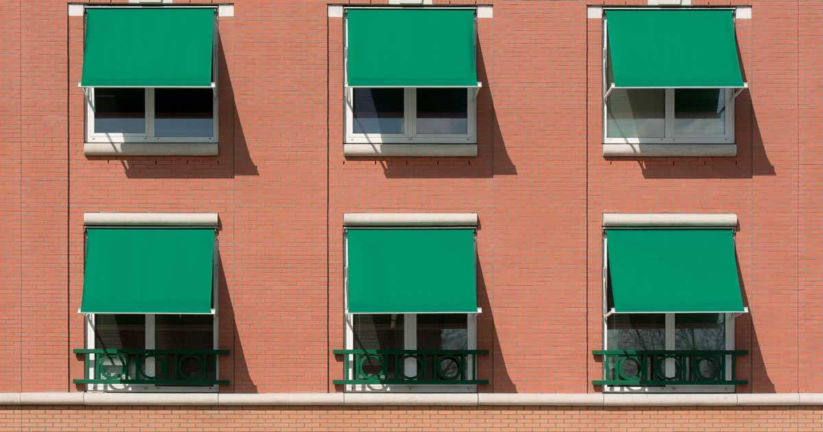 Bakstenen gevel met groene zonneschermen boven de ramen
