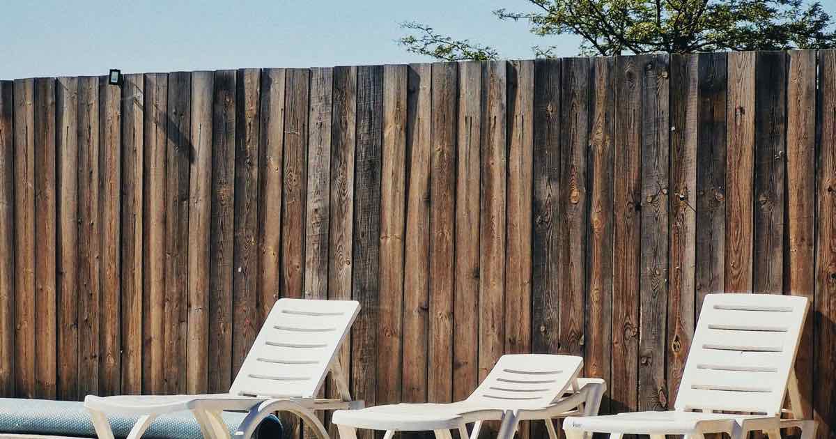 Ligstoelen bij een zwembad voor een houten schutting